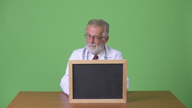 Handsome-senior-bearded-man-doctor-against-green-background