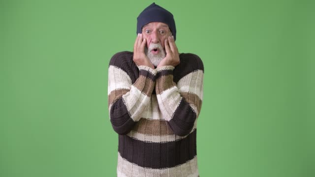 Gut-aussehend-Senior-bärtiger-Mann-in-warme-Kleidung-vor-grünem-Hintergrund