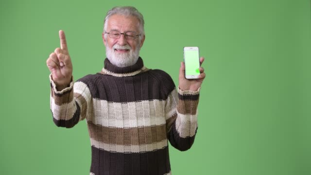 Gut-aussehend-Senior-bärtiger-Mann-in-warme-Kleidung-vor-grünem-Hintergrund