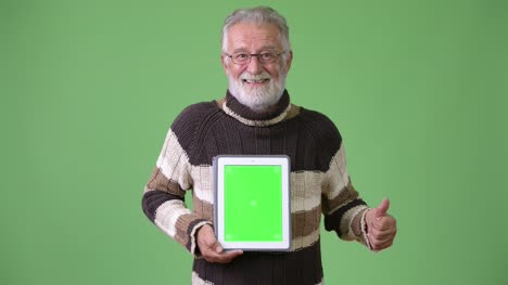 Handsome-senior-bearded-man-wearing-warm-clothing-against-green-background