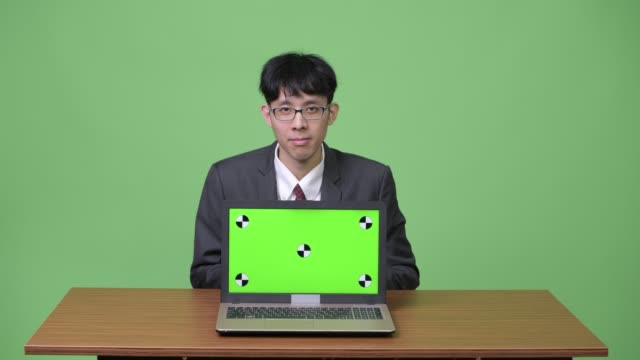 Joven-empresario-asiático-mostrando-portátil-para-cámara