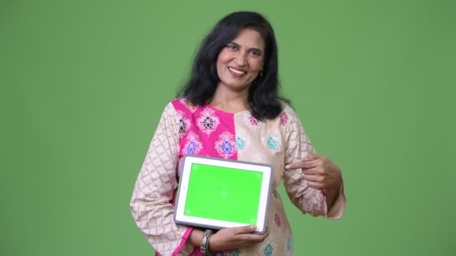 Mature-happy-beautiful-Indian-woman-showing-digital-tablet-and-pointing-finger