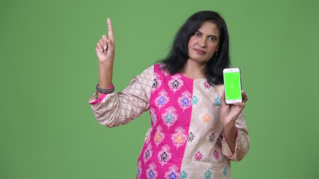 Madura-hermosa-mujer-India-mostrando-teléfono-y-apuntando-hacia-arriba