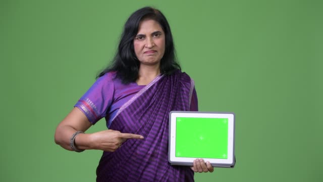 Mature-beautiful-Indian-woman-showing-digital-tablet-and-pointing-finger