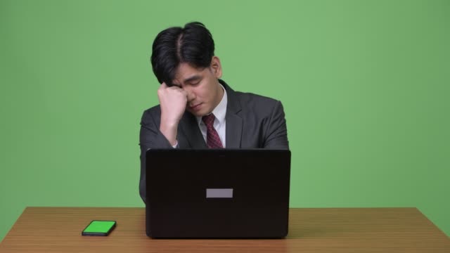 Junge-hübsche-asiatische-Geschäftsmann-arbeiten-mit-Laptop-vor-grünem-Hintergrund