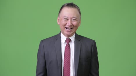 Reife-glücklich-japanischer-Geschäftsmann-lächelnd-vor-grünem-Hintergrund