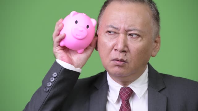 Mature-Japanese-businessman-holding-piggy-bank