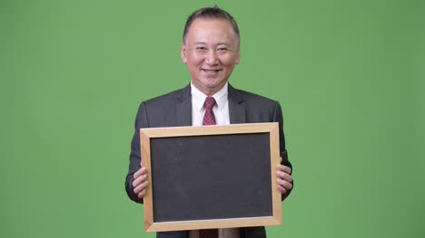 Reife-japanischer-Geschäftsmann-hält-Tafel-vor-grünem-Hintergrund