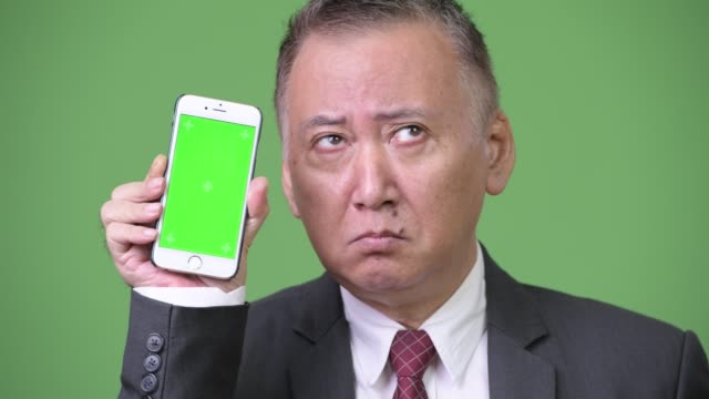 Mature-Japanese-businessman-showing-phone-to-camera
