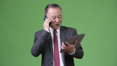 Reife-japanischer-Geschäftsmann-arbeiten-mit-digitalen-Tablet-und-Smartphone