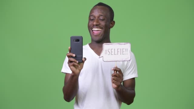 Joven-africana-tomando-selfie-con-signo-de-papel-sobre-fondo-verde