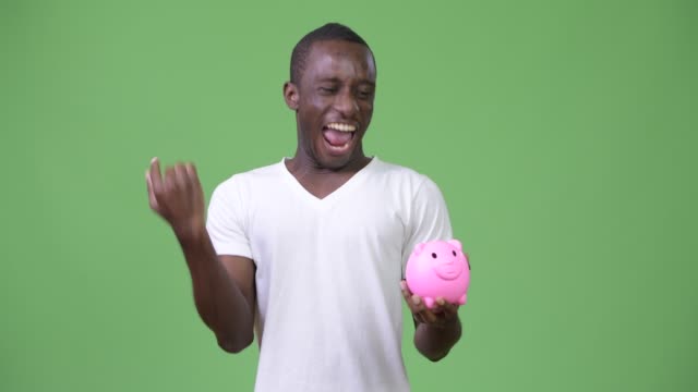 Young-African-man-holding-piggy-bank-and-giving-thumbs-up