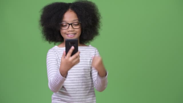 Young-cute-African-girl-with-Afro-hair-using-phone-and-celebrating