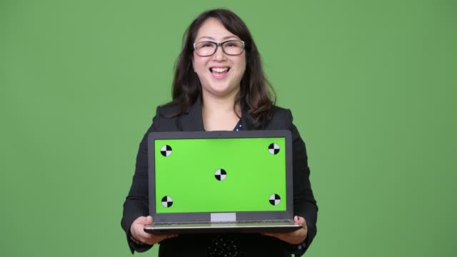 Madura-empresaria-asiática-hermosa-mostrando-portátil-sobre-fondo-verde
