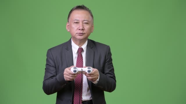 Mature-Japanese-businessman-playing-games-against-green-background