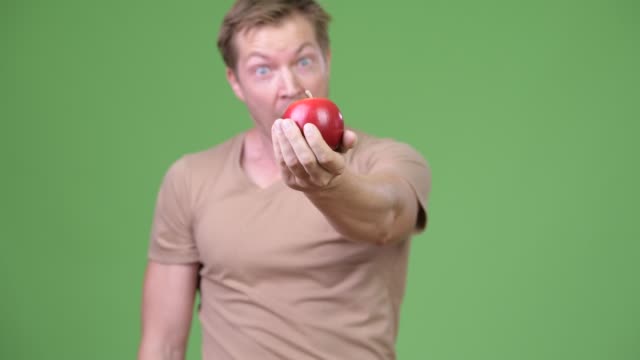 Young-handsome-Scandinavian-man-looking-shocked-while-holding-apple