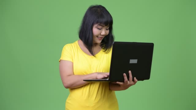 Schöne-glückliche-asiatische-Frau-denken-während-mit-laptop
