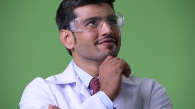 Young-handsome-Persian-man-doctor-wearing-protective-glasses-thinking