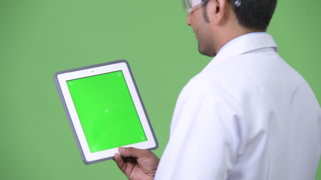 Young-handsome-Persian-man-doctor-wearing-protective-glasses-showing-digital-tablet