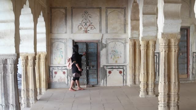 Woman-tourist-walking-around-pillars-columns-interior-architecture-traditional-Indian-motif-doors-wood-stone-handmade-ethnic-old-art-design-of-an-old-medieval-static-wide-shot-lock-down