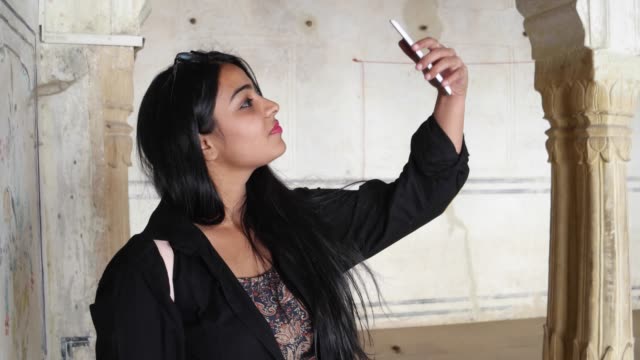 Pretty-woman-taking-photo-video-selfie-with-mobile-phone-camera-at-a-temple-old-ruin-building-interior-with-Indian-architecture-beautiful-handmade-admire-magnificent-handheld-arc-column-Rajasthan
