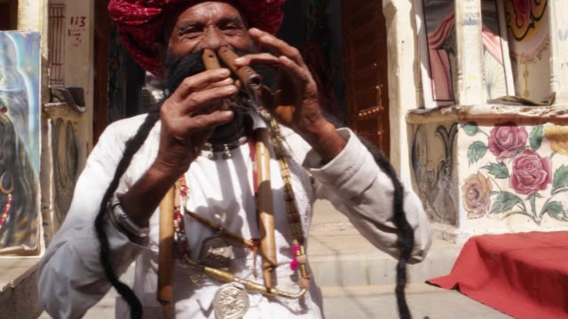 Mano-Rajasthani-ancianos-hombre-toca-la-flauta-con-la-nariz-delante-de-un-arco-del-templo-pintado,-con-gran-bigote-con-atuendos-tradicionales