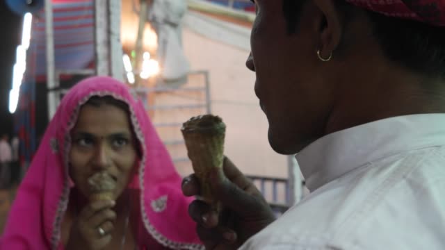 Indische-Paare-essen-Eis-in-traditionellen-Kleidern-im-Pushkar-Mela,-Karneval-von-Rajasthan,-Indien