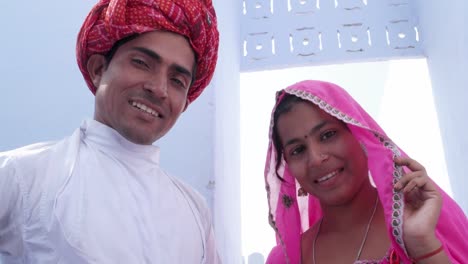 Handheld-Tilt-up-to-portrait-of-newly-wed-bride-in-pink-sari-and-groom-in-red-turban-walking-away-in-Rajasthan,-India
