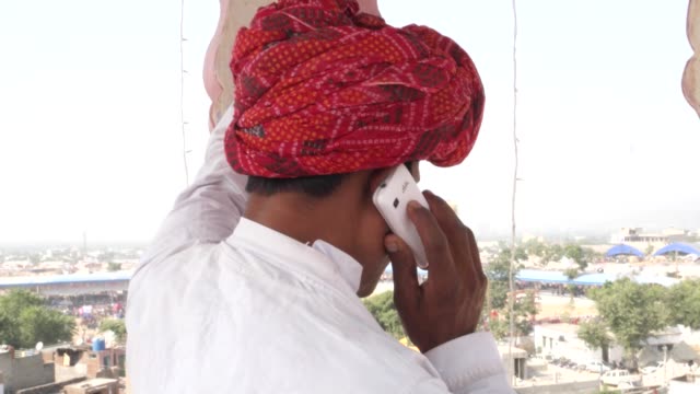 Nahaufnahme-eines-indischen-Mann-hektisch-auf-einem-Handy-Gespräch-auf-einem-Dach-in-traditioneller-Kleidung-in-Rajasthan,-Indien