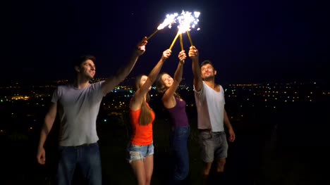 Die-vier-Menschen-stehen-mit-Feuerwerk-Sticks-auf-einem-Stadt-Hintergrund.-Nachtzeit