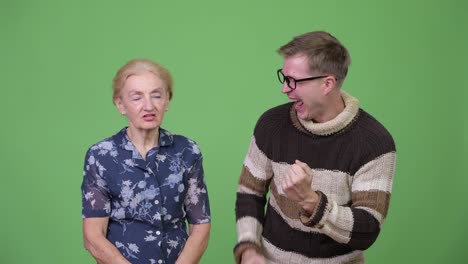 Grandson-celebrating-while-grandmother-looking-upset-against-green-background