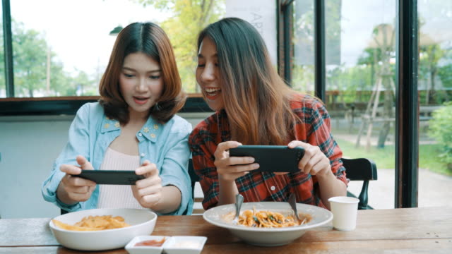 Glücklich-schöne-asiatische-Freunde-Frauen-Blogger-Smartphone-Fotos-und-Lebensmittel-Vlog-video-für-ihre-Abonnenten-und-ihrem-Kanal-im-Café.