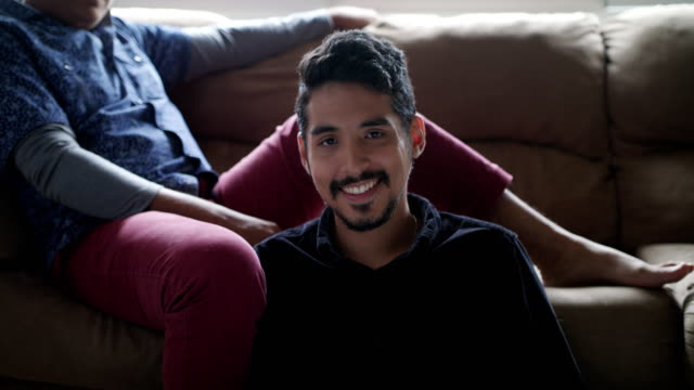 Hispanic-Pareja-Gay-Holding-Hands-On-sofá-en-casa
