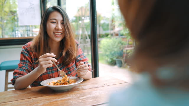 Schöne-glückliche-asiatische-Frauen-Lesben-LGBT-paar-sitzt-jeder-Seite-einen-Teller-mit-italienischen-Meeresfrüchte-Spaghetti-und-Pommes-frites-in-Restaurant-oder-Café-zu-essen,-während-lächelnd-und-Blick-auf-Lebensmittel.