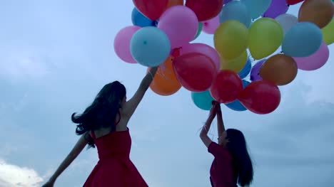 Two-girls-holding-balloon-with-sky-background-in-slow-motion.