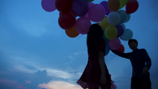 Young-couple-people-holding-balloon-with-sunset-background-in-slow-motion.