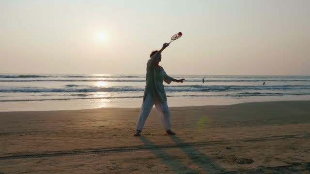Ältere-Frau-praktizieren-Tai-Chi-Ballon-Ball-am-Strand-bei-Sonnenuntergang