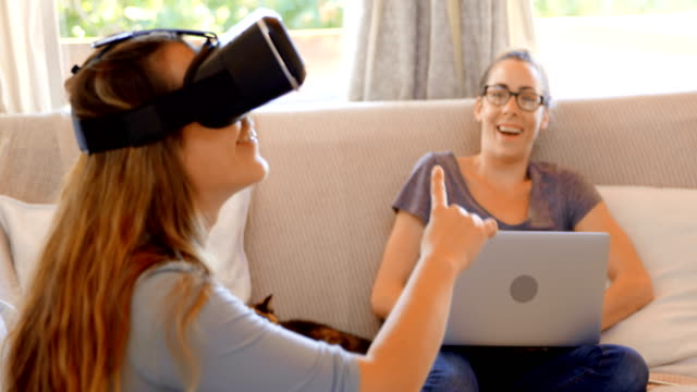 Lesbisches-Paar-mit-virtual-Reality-Kopfhörer-und-Laptop-im-Wohnzimmer-4k
