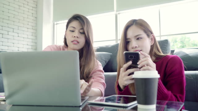 Lesbian-Asian-couple-using-laptop-making-budget-in-living-room-at-home,-sweet-couple-enjoy-love-moment-while-lying-on-the-sofa-when-relax-at-home.-Lifestyle-couple-relax-at-home-concept.