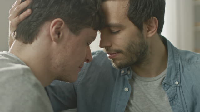 Cute-Male-Queer-Couple-Put-Their-Heads-Together-and-Close-Their-Eyes.-Sweet-Gentle-Loving-Gay-Relationship-Moment.-Room-Has-Modern-Interior.