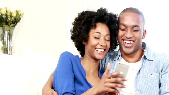 Glückliches-junges-Paar-sitzen-auf-dem-Sofa,-während-Sie-eine-SMS-Freundin-ist