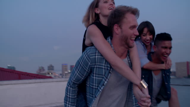 Hipster-fun-loving-friends-doing-piggyback-rides-on-rooftop