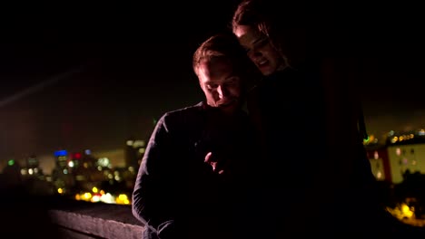 Junges-Paar-schaut-an-Smartphone-auf-Dach-bei-Nacht