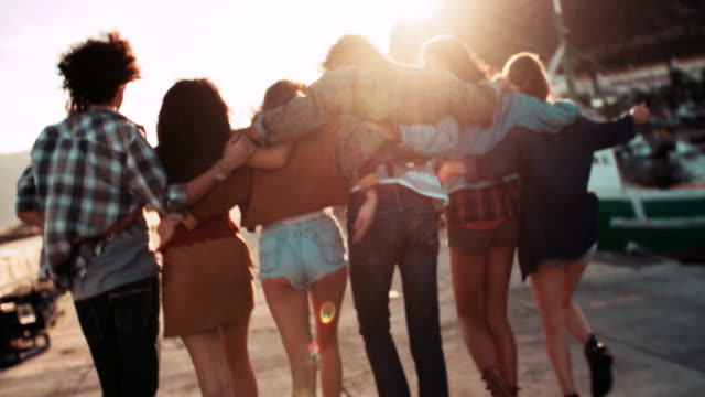 Teen-hipster-Freunde-zu-Fuß-auf-dem-Anlegestelle-ein-Sonnenuntergang
