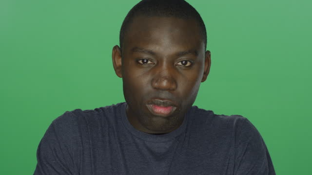 Young-African-American-man-glares,-on-a-green-screen-studio-background