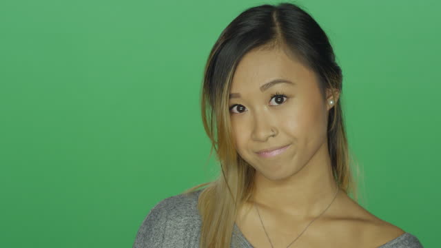 Cute-Asian-girl-looking-sad-and-then-smiling,-on-a-green-screen-studio-background