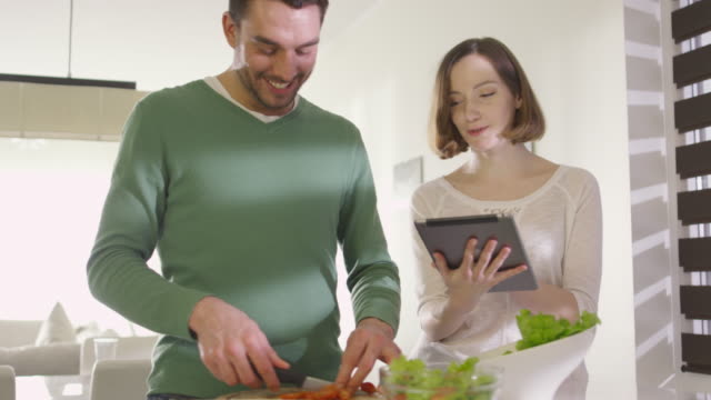 Happy-couple-is-preparing-healthy-food-in-the-kitchen-at-home-while-checking-a-tablet-computer.