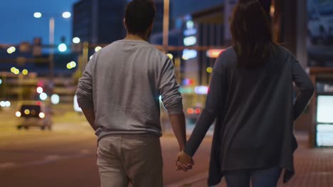 Seguir-a-tiro-de-la-atractiva-pareja-feliz-caminando-por-las-calles-de-la-ciudad-de-noche