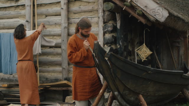 Leben-der-zivilen-Menschen-im-Dorf.-In-mittelalterliche-Kleidung-Mann-macht-ein-Boot-während-Frau-hängt-Kleidung-gekleidet.--Mittelalterlichen-Reenactment.