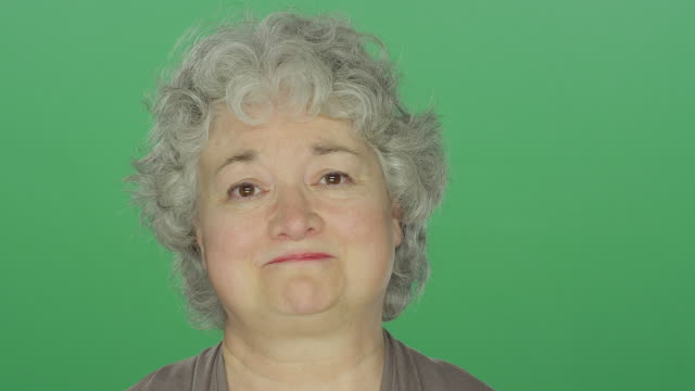 Older-woman-looking-slightly-sad,-on-a-green-screen-studio-background